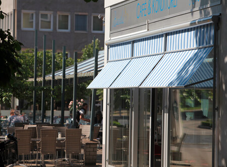Blau- weiß gestreifte Markisoletten als Sonnenschutz bei freier Durchsicht an der großflächigen Fensterfront eines Cafés