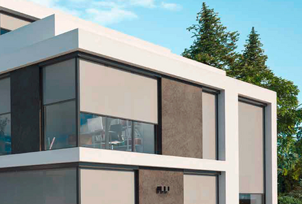 Ansicht einer modernen Einfamilienhausfront mit vielen Fenstern, mit heruntergefahrenem Zip Screen Sonnenschutzsystem in lichtgrau