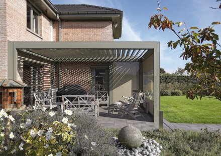 Terrassenüberdachung in grau mit halbgeöffneten Dachlamellen über der Terrasse eines Einfamilienhauses