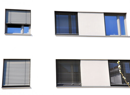 Fassade eines öffentlichen Gebäudes mit Außenjalousien jeweils eine Jalousie über vier bzw. fünf nebeneinander liegende Fenstern, teilweise herunter gelassen.