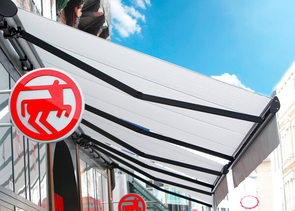 Ladenmarkise in weiß mit antrazitfarbenden Metallstützen als Sonnenschutz für den Laden und die Aussenware