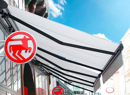 Ladenmarkise in weiß mit antrazitfarbenden Metallstützen als Sonnenschutz für den Laden und die Aussenware